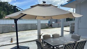 Eine Terrasse im Freien mit Tisch, Stühlen und einem großen Sonnenschirm, mit einem Betonboden.