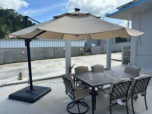 Eine Terrasse im Freien mit Tisch, Stühlen und einem großen Sonnenschirm, mit einem Betonboden.