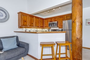 Une cuisine compacte dotée de meubles en bois, d’un four à micro-ondes, d’un réfrigérateur et d’un petit coin bar avec des tabourets.