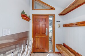 Une porte en bois avec un panneau de verre, un banc, une étagère fixée au mur et une fenêtre au-dessus de la porte.