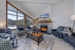 A spacious living room with a stone fireplace, large windows, and a cozy seating area. - Blackcomb Greens #4 - Mountain View, Right on the Golf Course! (Whistler)