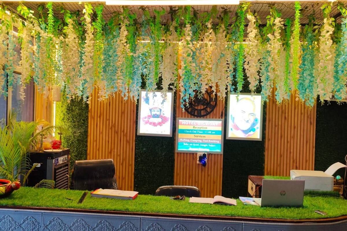 A reception desk with a laptop, a wooden backdrop, and hanging plants.