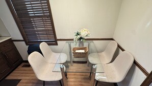 A dining area with a glass table, two beige chairs, a wicker basket, and a vase with flowers. - Modern 2BR Suite 202: Toledo & Sylvania Gateway (Toledo)