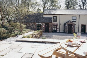A stone building with a paved patio and a wooden table with food and drinks. - The Byre Lake District Retreat By Together Travel (Penrith)