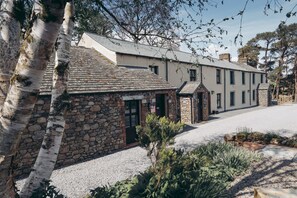 A stone building with a sloped roof, a stone entrance, and a gravel driveway. - The Byre Lake District Retreat By Together Travel (Penrith)