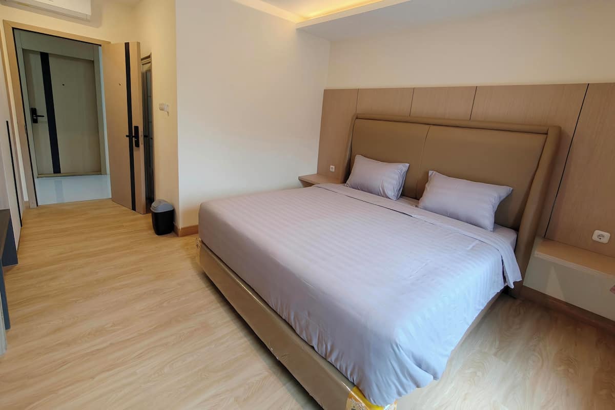 A modern bedroom with a large bed, wooden flooring, and a built-in headboard.