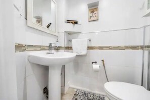 A bathroom with a white sink, toilet, and a mirror.