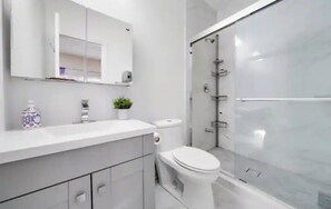 A modern bathroom with a white vanity, a toilet, and a glass-enclosed shower.