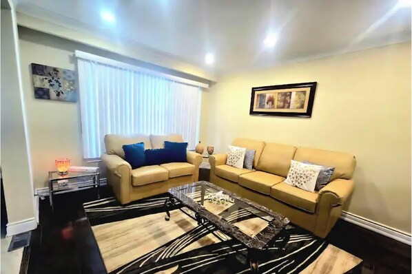 A living room with two beige sofas, a glass coffee table, a striped rug, a side table with a lamp, and a framed picture on the wall.