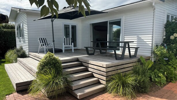 Une maison blanche dotée d’une terrasse en bois, d’un espace salon extérieur et d’un patio couvert.