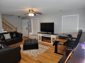 A living room with a black leather sofa, a wooden coffee table, a TV, a fireplace, and a ceiling fan.