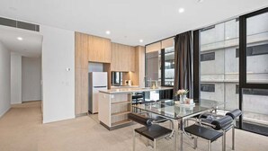 A modern kitchen with a glass dining table and chairs, a built-in oven, and a view of the city through large windows. - Level 10 Views | 2BR with Private Balcony & Parking (Brisbane)