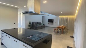 Una cocina moderna con una isla central, un comedor con mesa y sillas, y una sala de estar con sofá y televisor.