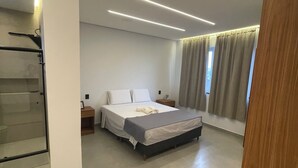 Un dormitori modern amb un llit, una taula de nit i vista a l'exterior a través d'una finestra amb cortines.