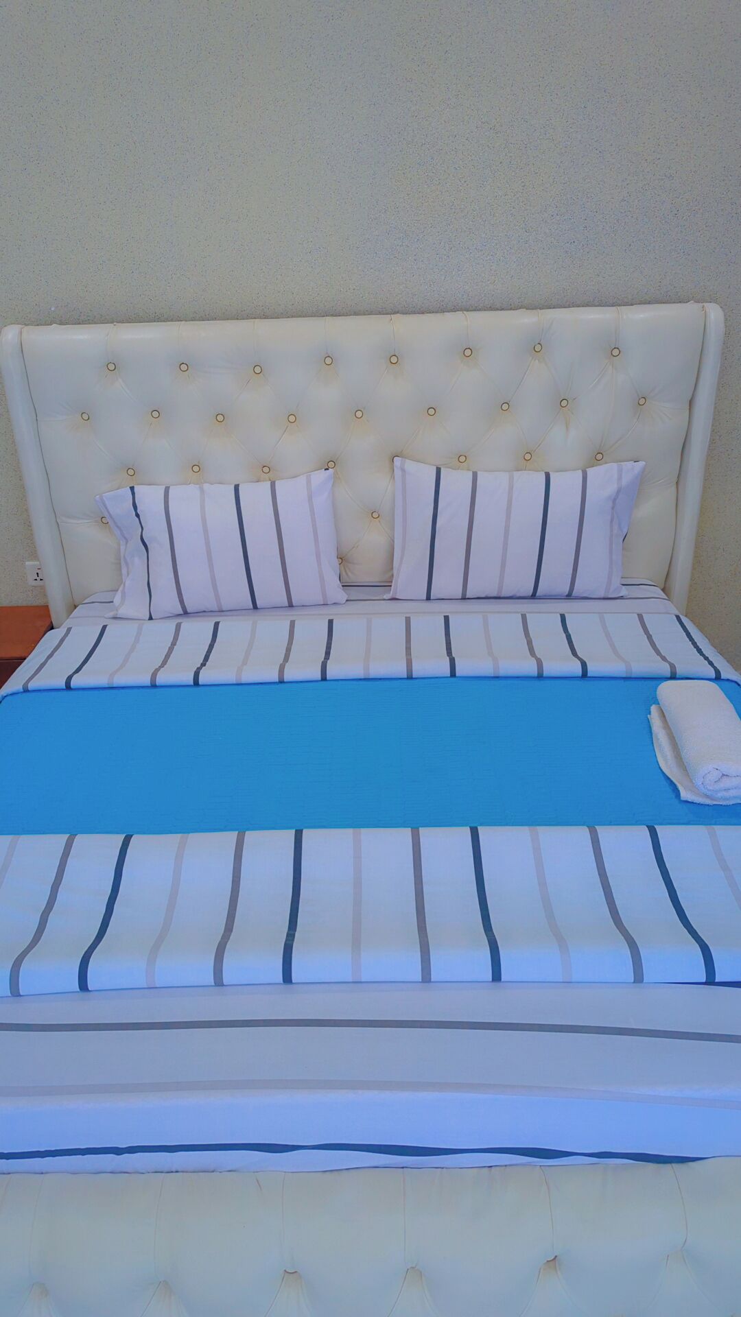 A bed with a tufted headboard, striped bedding, and a folded towel.