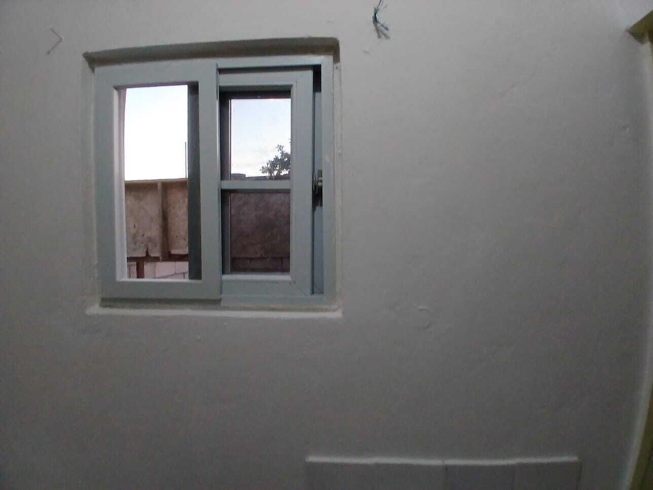 Une pièce avec une petite fenêtre, des murs sobres et une porte bien visible.