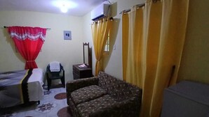 Une pièce comprenant un lit, un canapé, une chaise, une petite table et un climatiseur fixé au mur.
