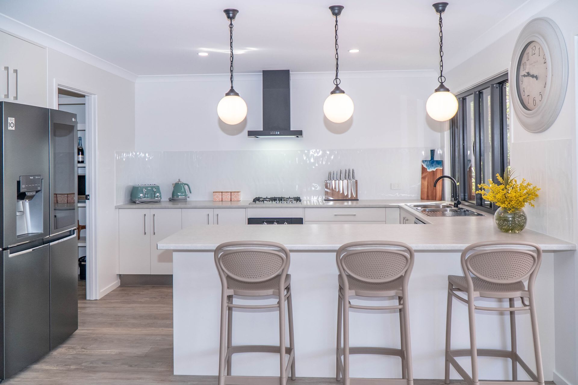 A modern kitchen with a central island, bar stools, a refrigerator, and a clock on the wall.
