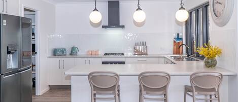A modern kitchen with a central island, bar stools, a refrigerator, and a clock on the wall.