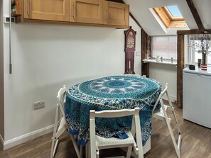 A round table with a patterned tablecloth, a wooden cabinet, a clock, and a skylight. - 2 bedroom accommodation in Mousehole, near Penzance (Mousehole, near Penzance)