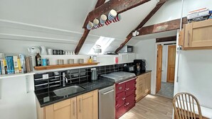 Une cuisine avec un plan de travail noir, des placards en bois, un four rouge et une chaise en bois.