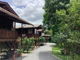 Um edifício de madeira tradicional com galeria coberta e um caminho de cascalho serpenteando por um jardim exuberante.