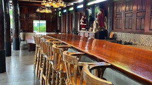 A long wooden bar with high stools, wooden paneling, and hanging chandeliers. - The Elephant House and Pool Villas (San Pa Thong)