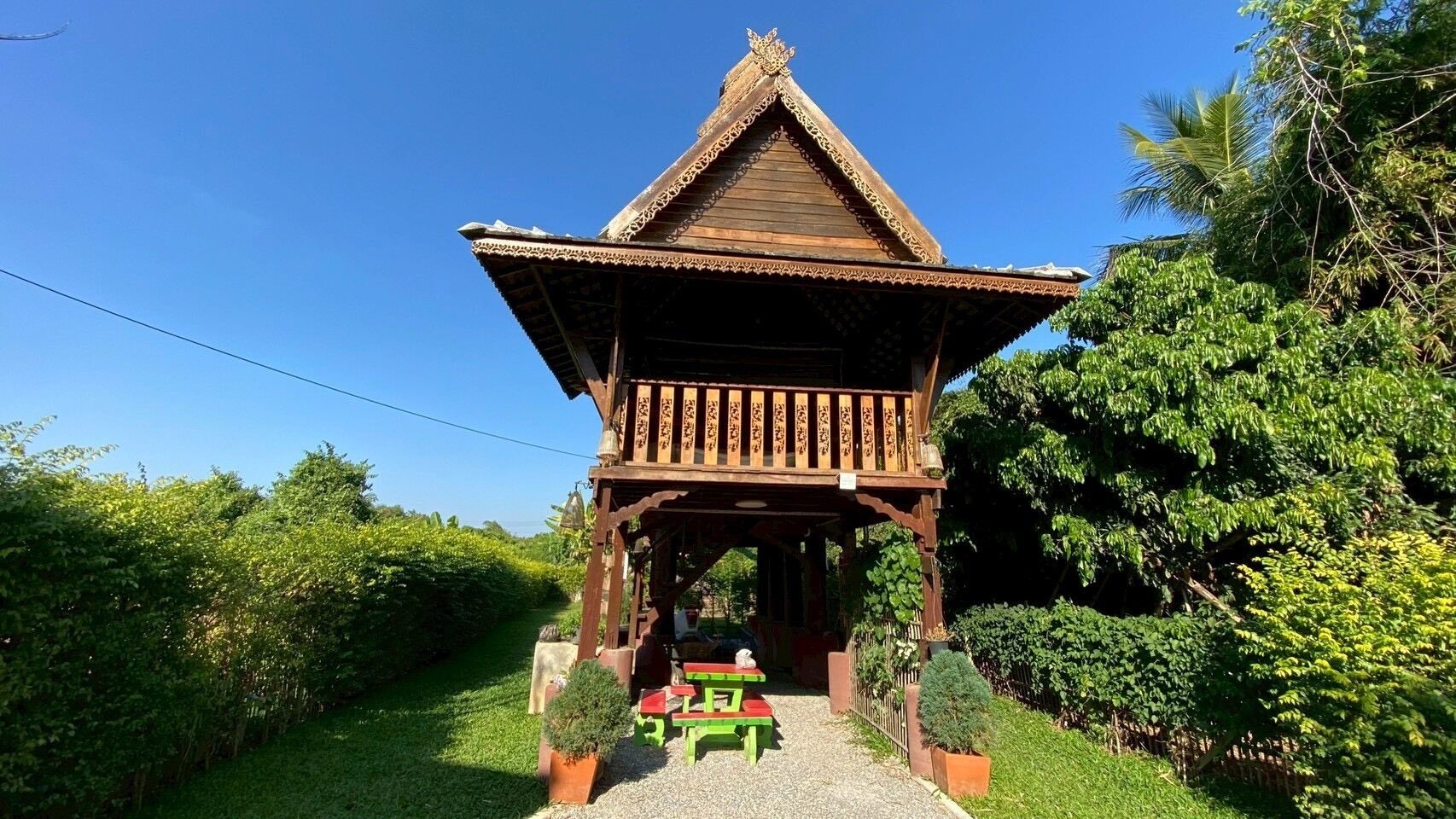 Une construction traditionnelle en bois, surmontée d’un toit en tuiles, et entourée d’une végétation luxuriante.