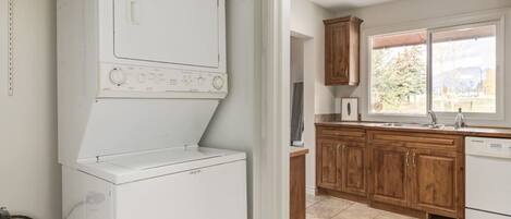 A laundry area with a washing machine and dryer, wooden cabinets, a window with a view, and a tiled floor.