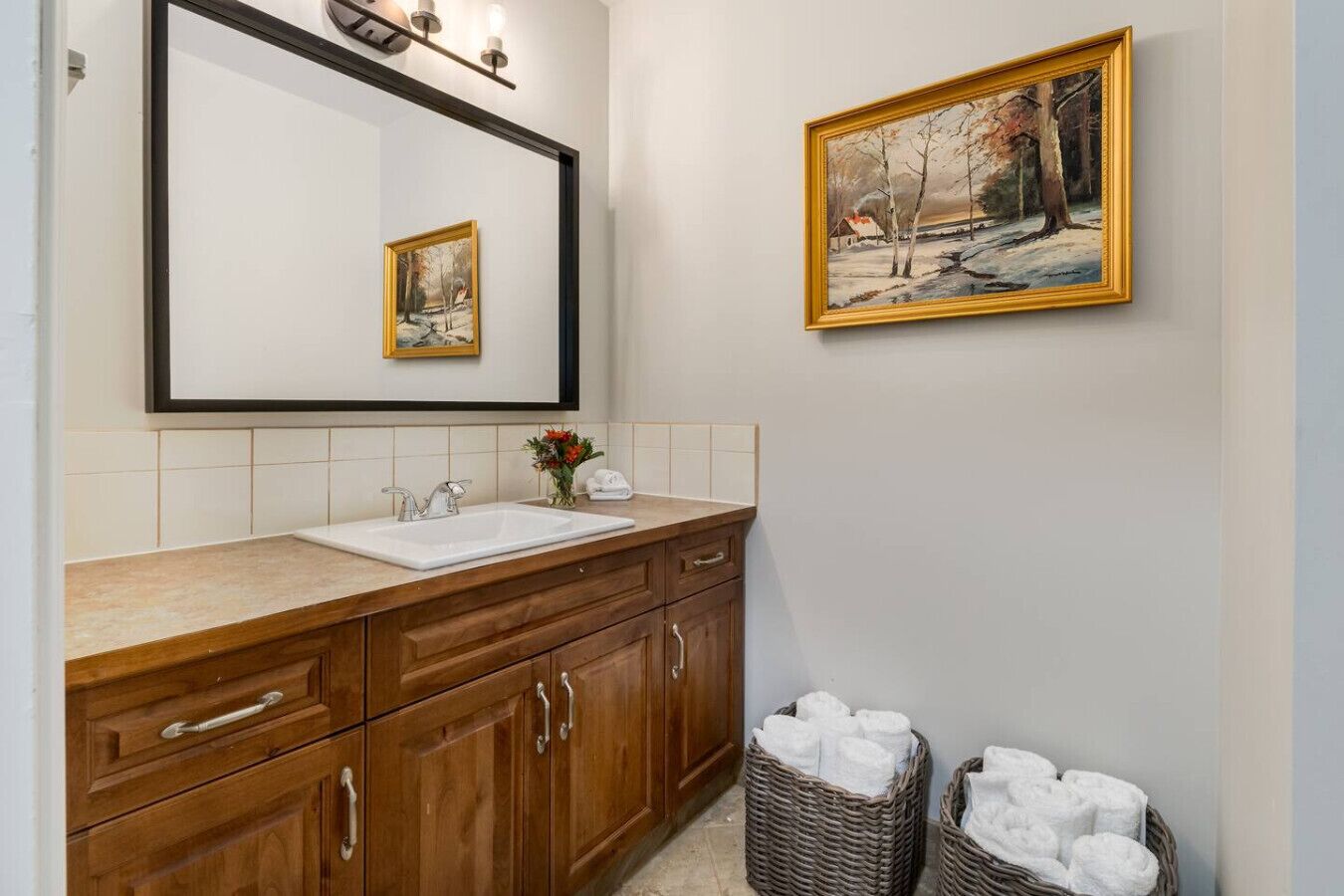 Un baño con tocador de madera, un lavamanos blanco, un espejo y un cuadro en la pared.