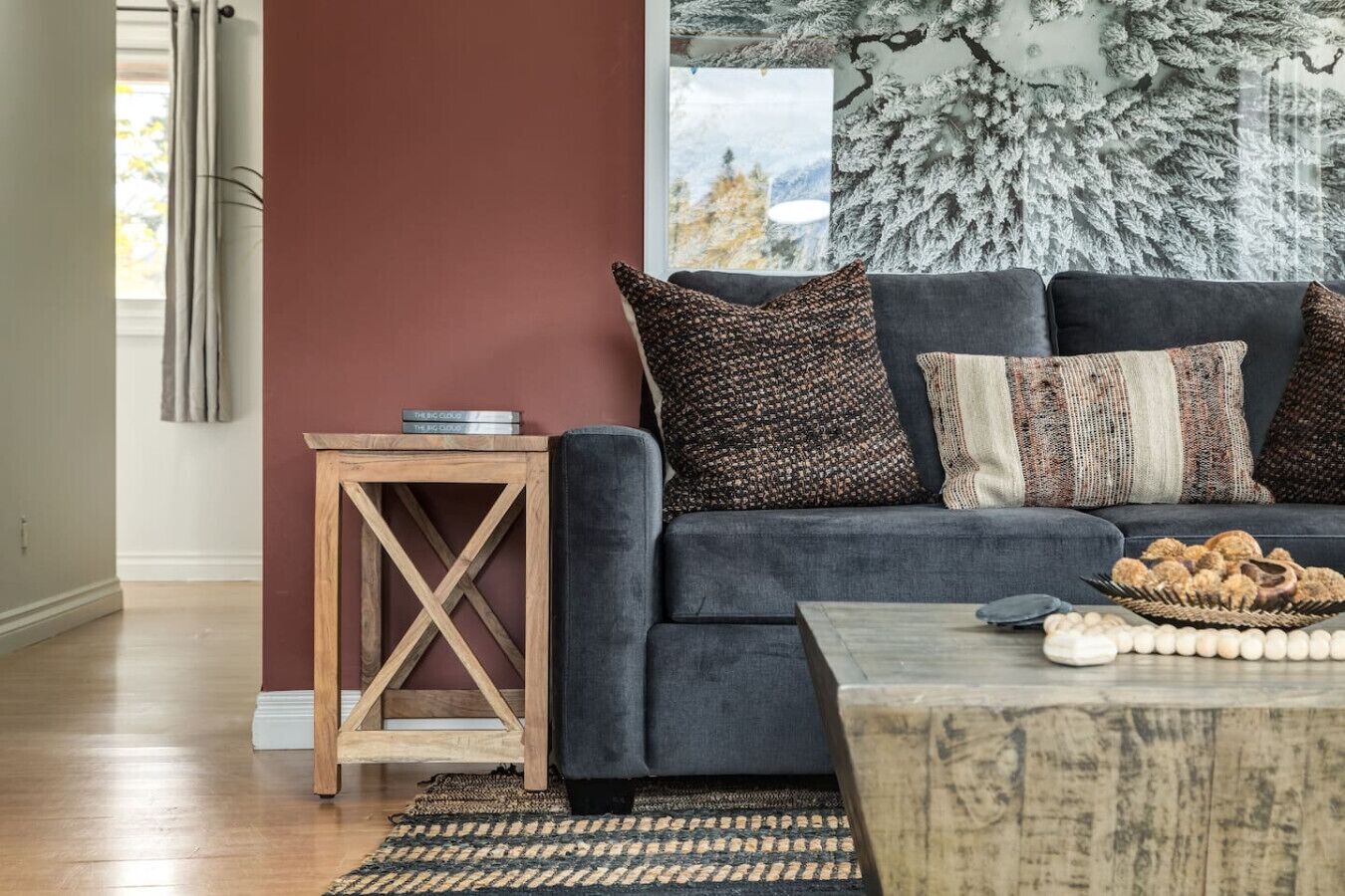 Una sala de estar moderna con un sofá gris, cojines estampados, una mesita de madera y una mesa de centro con productos horneados.