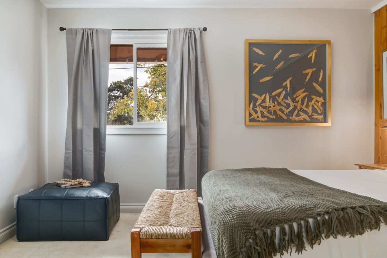 A bedroom with a bed, a bench, a small ottoman, and a window with curtains.