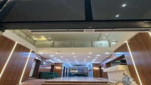 Een ruime lobby met een centrale trap, een receptiebalie en een hoog plafond met inbouwverlichting.
