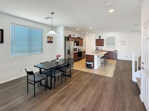 A modern kitchen with wooden flooring, a dining area with a table and chairs, and a small island with stools. - 4BR Casa Grande Home | Game Table + Large Yard (Casa Grande)