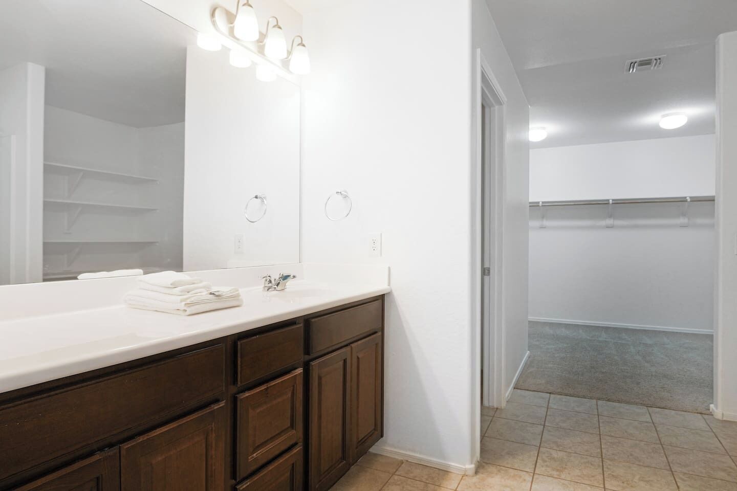 A bathroom with a large mirror, a vanity with a sink, and a walk-in closet.