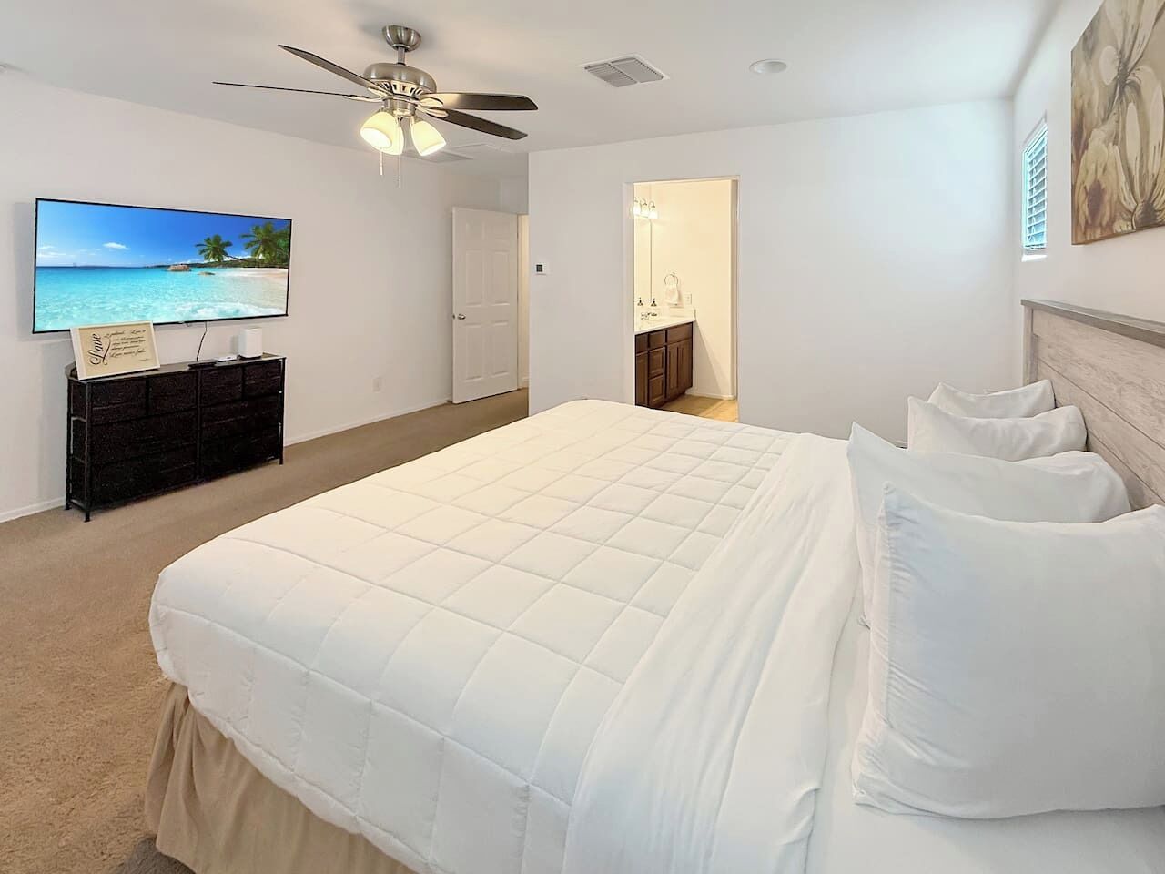 Ein Schlafzimmer mit einem großen Bett, einem Deckenventilator, einem Fernseher und einer Tür zu einem Badezimmer.