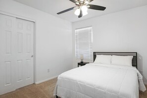 A bedroom with a bed, a ceiling fan, a nightstand, and a window with blinds. - 4BR Casa Grande Home | Game Table + Large Yard (Casa Grande)