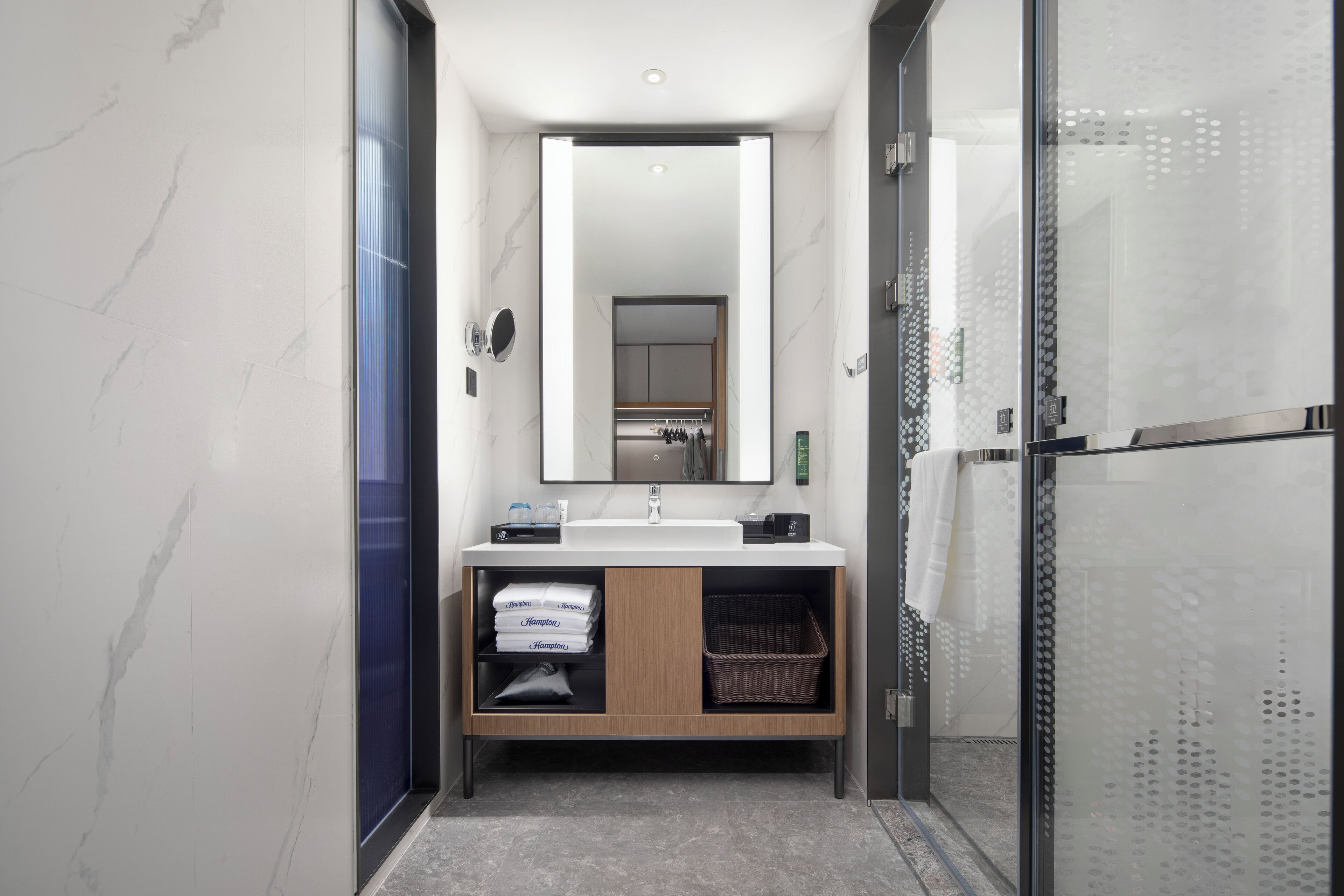 A modern bathroom with a marble wall, a large mirror, a sink, and a glass shower enclosure.