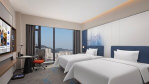 Une chambre d’hôtel avec deux lits, un bureau, une chaise et une grande fenêtre donnant sur la ville.