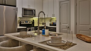 Cozinha moderna com armários brancos, eletrodomésticos de aço inoxidável e uma ilha central com utensílios de mesa.