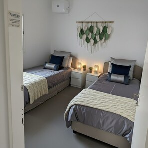 A bedroom with two single beds, bedside tables with lamps, a wall-mounted plant, and a whiteboard. - New 2-bedroom apartment in Jerusalem for relaxing stays (Jerusalem)