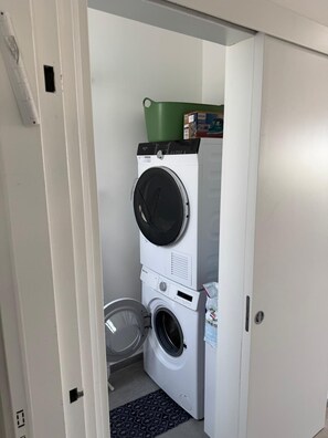 A laundry room with stacked washers and dryers, a green trash bin, and a white door. - New 2-bedroom apartment in Jerusalem for relaxing stays (Jerusalem)