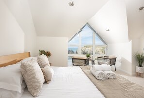 A bedroom with a large bed, a view of the sea, and a small table with a chair. - Seaside House is an exceptional coastal retreat offering panoramic views (Portreath)