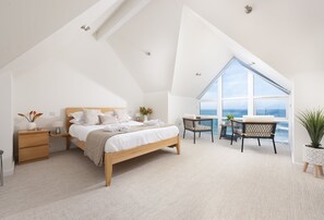 Ein modernes Schlafzimmer mit einem großen Bett, einem Schreibtisch und Meerblick durch ein großes Fenster.