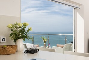 Ein Balkon mit Meerblick, eine weiße Vase mit Blumen, eine Kamera und ein gewebter Korb.