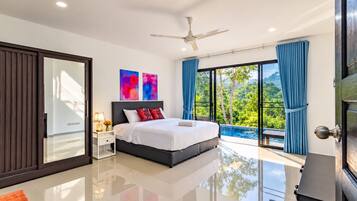 A modern bedroom with a large bed, a ceiling fan, and a view of a lush garden through floor-to-ceiling windows.