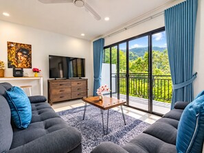 A modern living room with a flat-screen TV, a wooden cabinet, and a balcony with a view of greenery. - Brand New Private pool villa Chalong Phuket Mountain view (Tambon Chalong)