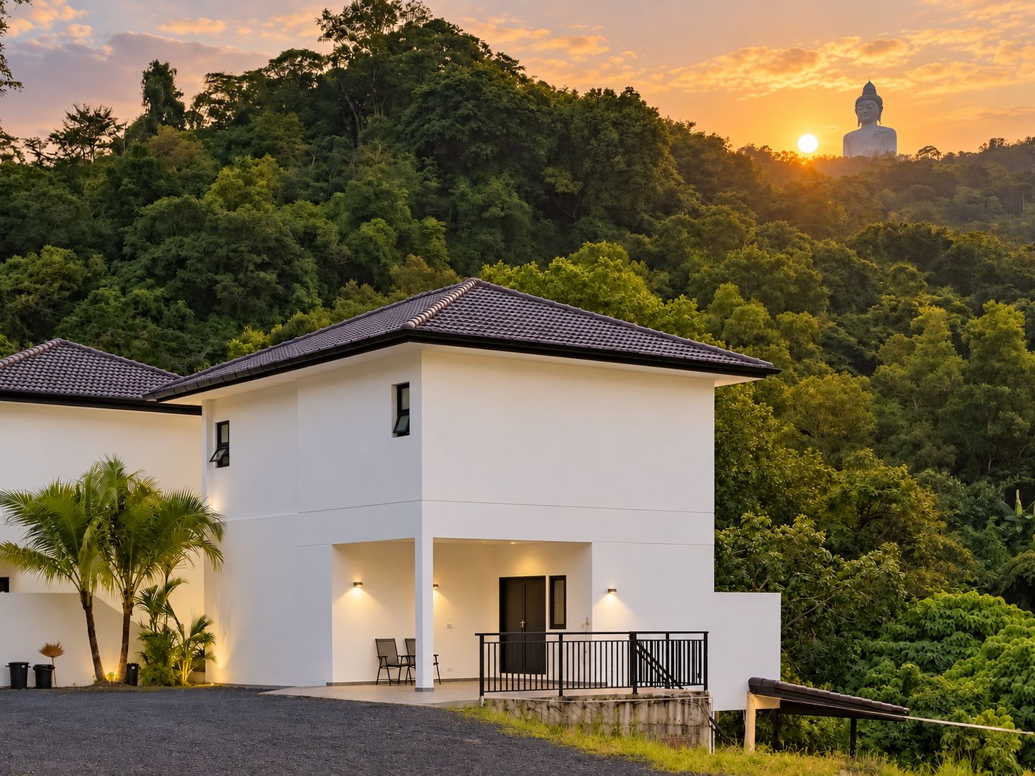 A modern two-story building with a flat roof, a balcony, and a view of a large Buddha statue in the background.