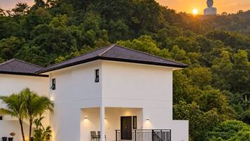A modern two-story building with a flat roof, a balcony, and a view of a large Buddha statue in the background.