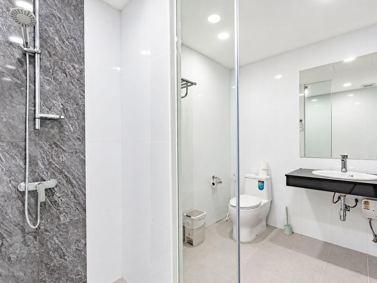 Un baño moderno con cabina de ducha de vidrio, inodoro blanco y lavamanos con espejo superior.